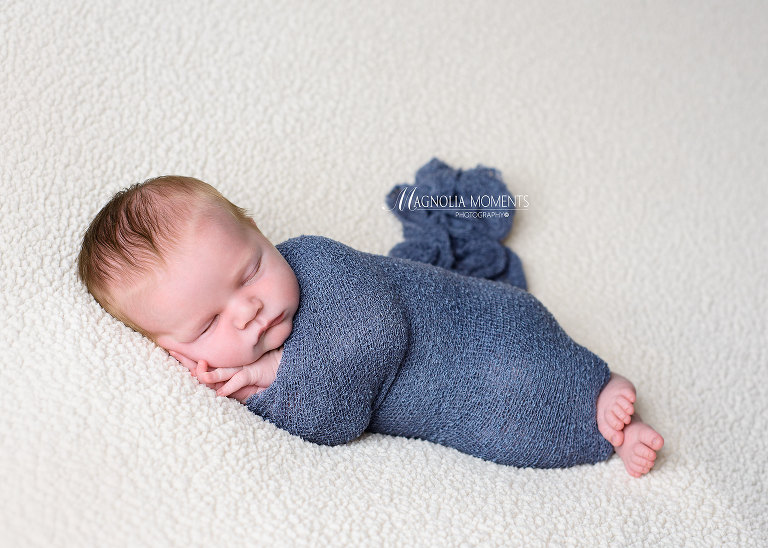 Newborn boy posed on his side and wrapped in blue during his newborn photography session by Evan Pollock of Magnolia Moments Photography