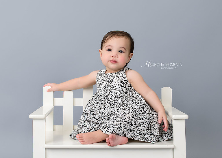 1st birthday photography session of adorable girl on white bench in adorable cake smash outfit