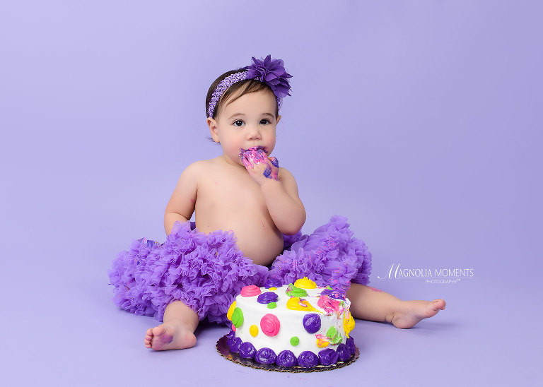 adorable baby girl on purple tasting her smash cake during her 1st birthday cake smash session by Evan Pollock of Magnolia Moments Photography