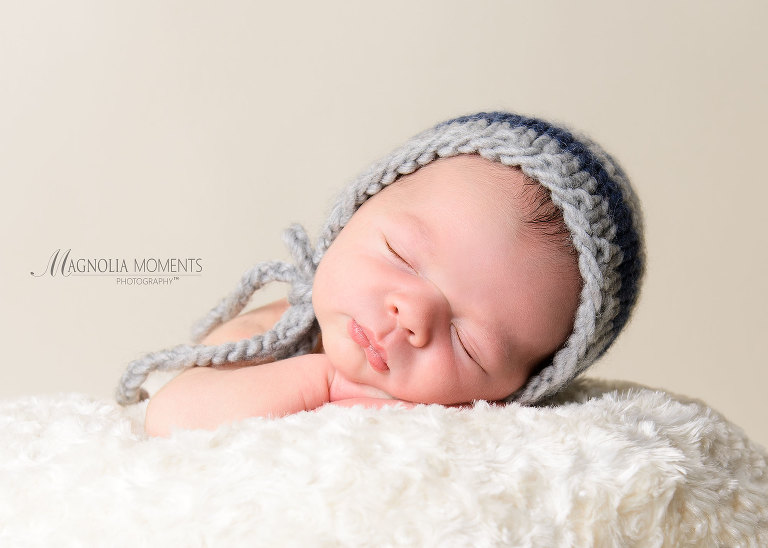 Closeup of newborn boy in grey hat on cream blanket photographed by Evan Pollock of Magnolia Moments Photography who does professional photography near me. Yardley newborn photographer