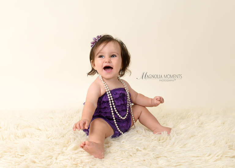 1 year old baby girl in purple seated on fur during her first birthday smash cake session by Magnolia Moments Photography one of the photographers near me