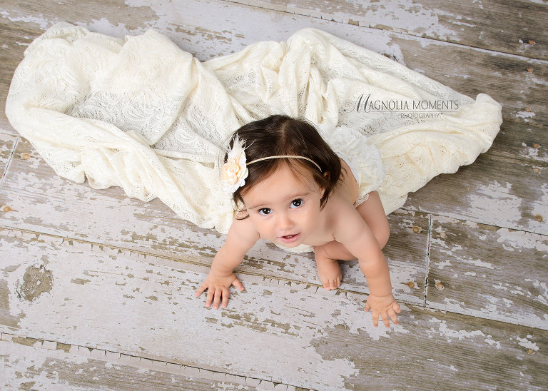 One year old baby girl on barn floor during her first birthday cake smash portrait session by Magnolia Moments Photography