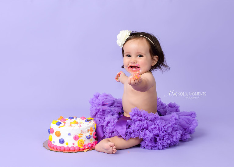 Baby girl in purple tutu with birthday cake on lavender backdrop during her cake smash session by Magnolia Moments Photography one of the professional photographers near me
