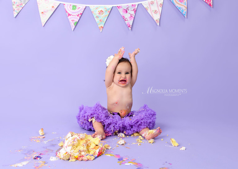 Baby girl in purple tutu with smash birthday cake on lavender backdrop for her first birthday cake smash session by Evan Pollock of Magnolia Moments Photography
