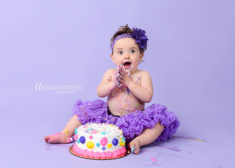 One year old baby girl delighted with her birthday cake and dressed in purple tutu for her cake smash outfit for her 1st birthday portrait session by Evan Pollock of Magnolia Moments Photography in PA