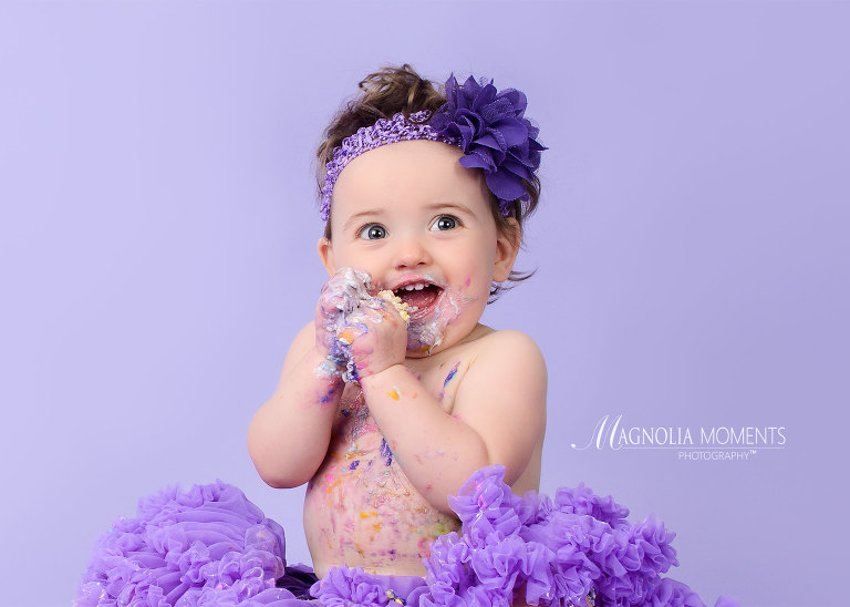 Girl in purple tutu during her first birthday cake smash session by Evan Pollock of Magnolia Moments Photography who does professional photography near me