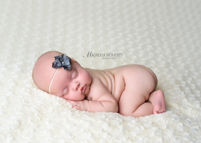 Baby girl posed on white blanket with grey flower photographed by Evan Pollock of Magnolia Moments Photography on of the photography studios near me