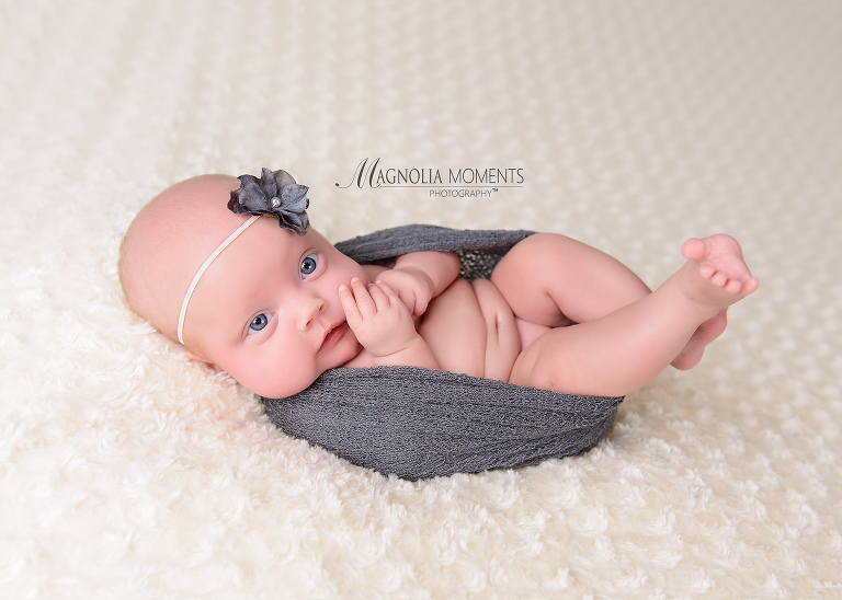Newborn baby girl with big blue eyes wrapped in grey during her newborn photography session by Evan Pollock and Magnolia Moments Photography