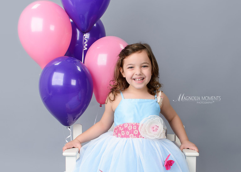 Birthday girl in pretty blue dress with purple and pink balloons during her birthday photography session by Magnolia Moments Photography a professional photographer near me. Collegeville child photographer.