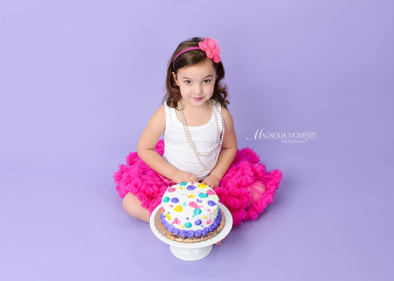 Birthday girl seated with cake on lavender background wearing pink tutu during her birthday portrait session by Evan Pollock of Magnolia Moments Photography one of the photographers near me. Collegeville child photographer.