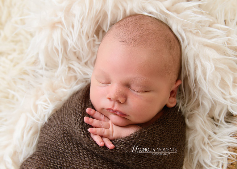 Sweet newborn baby boy wrapped in brown with hands under chin during his newborn photography session by Evan Pollock of Magnolia Moments Photography a professional photographer near me. Gilbertsville newborn photographer