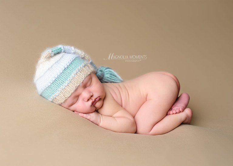Newborn boy in stripped hat on tan brown backdrop for his newborn photo shoot by Evan Pollock of Magnolia Moments Photography.Gilbertsville newborn photographer