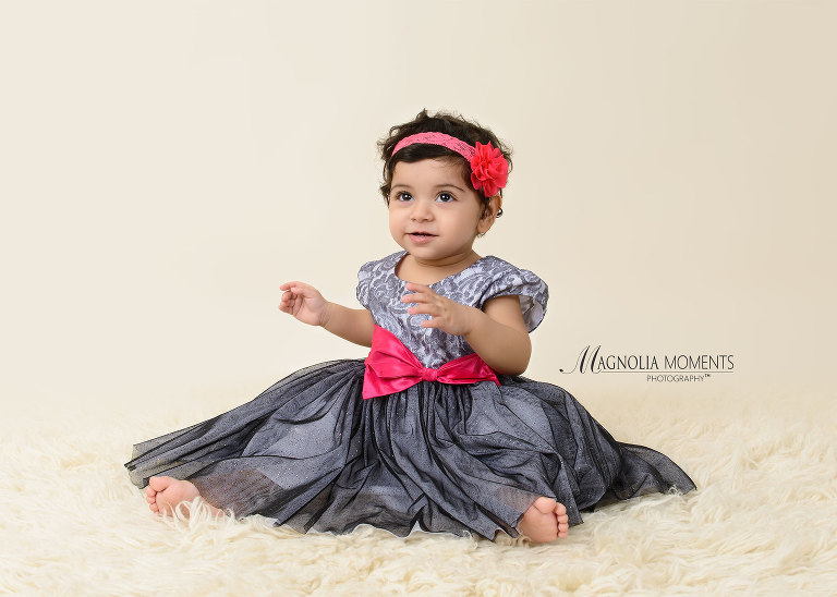 Adorable birthday girl dressed in grey dress with pink bow for her cake smash outfit in her 1st birthday cake smash by Evan Pollock of Magnolia Moments Photography on of the photography studios near me. Lansdale child photographer