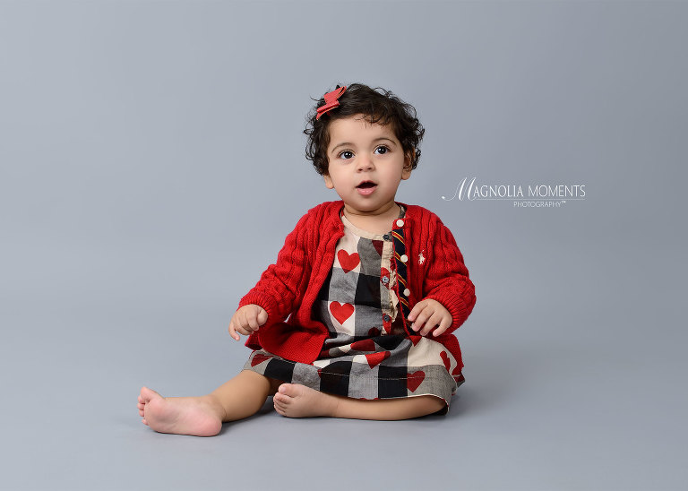 one year old girl in red sweater on grey background during her 1st birthday cake smash by Evan Pollock of Magnolia Moments Photography one of the photographers near me. Lansdale child photographer