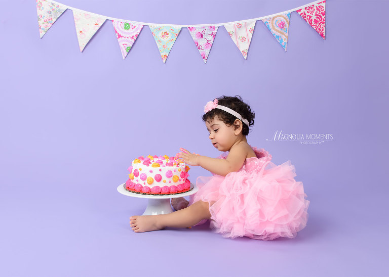 Baby girl in pink tutu on lavender backdrop with birthday cake during her cake smash by Evan Pollock a professional photographer near me. Lansdale child photographer