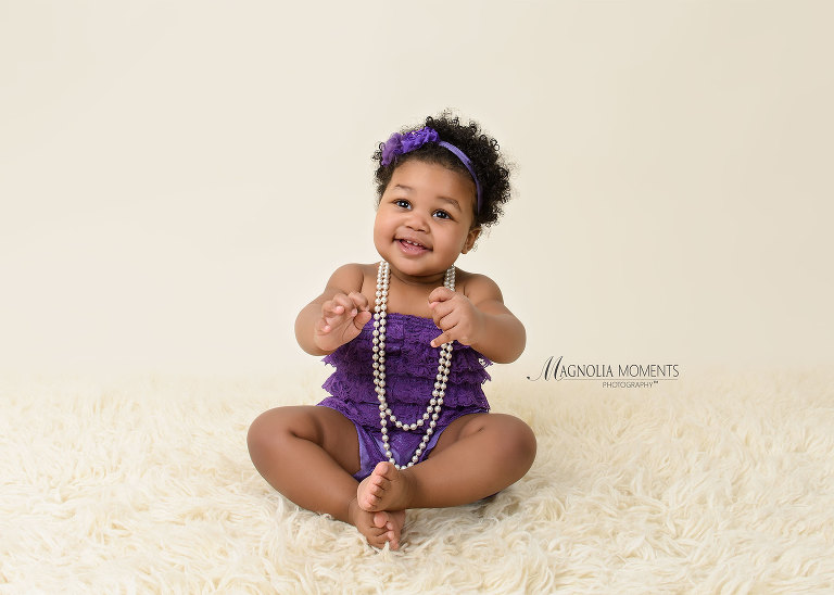 Adorable 1 year old baby girl in purple romper during her 1st birthday cake smash by Evan Pollock of Magnolia Moments Photography, Collegeville PA Cake Smash photographer.