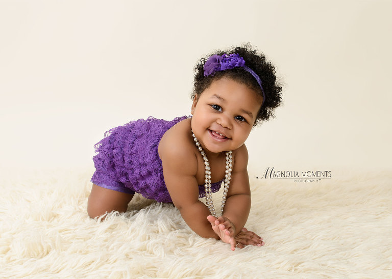 Sweet baby girl in purple romper photographed by Evan Pollock of Magnolia Moments Photography during her 1st birthday cake smash.