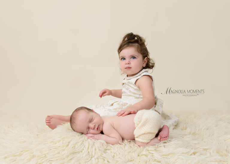 Newborn baby boy with big sis posed on cream fur by Evan Pollock of Magnolia Moments Photography who does professional photography near me. Blue Bell newborn photographer.