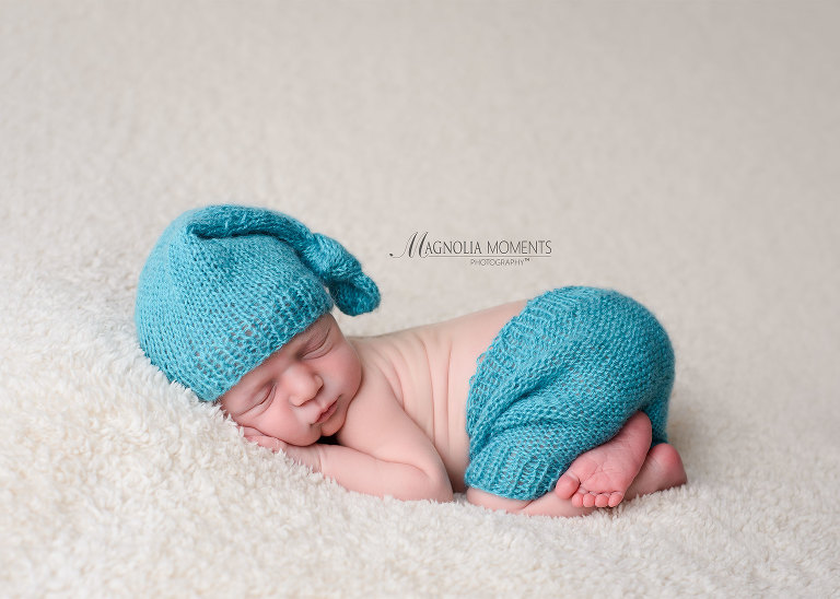 Sweet newborn boy in blue sleepy hat and shorts on cream photographed by Evan Pollock of Magnolia Moments Photography a newborn photographer near me. Blue Bell newborn photographer.