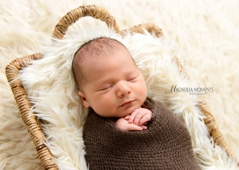 Newborn boy wrapped in brown with hands posed under chin for his newborn portraits by Evan Pollock of Magnolia Moments Photography one of the photographers near me.