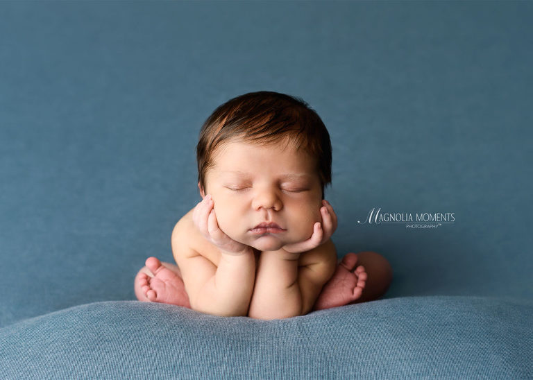 Adorable newborn boy with chin in hands on blue blanket by Evan Pollock of Magnolia Moments Photography who does newborn photography near me. King of Prussia newborn photographer.