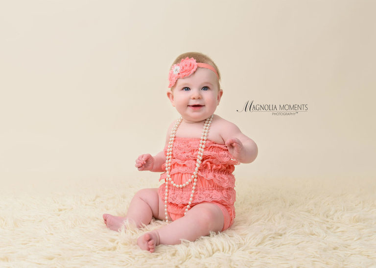 6-month baby girl in pink romper and headband and pearls on cream fur during her baby photography session by Evan Pollock of Magnolia Moments Photography a photography studio near me. Mont Clare baby photographer.