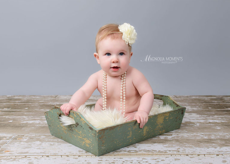 Baby girl in green box on barn floor during her baby portrait session by Evan Pollock of Magnolia Moments Photography who does professional photography near me. Mont Clare baby photographer.