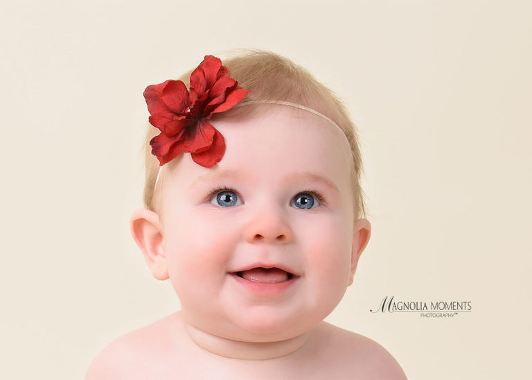 Close of 6-month old baby girl wearing red flower headband in her baby photography session by Evan Pollock of Magnolia Moments Photography a professional studio near me. Mont Clare baby photographer.