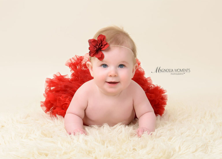 Baby girl in red tutu and flower headband laying on cream fur during her baby photography session by Evan Pollock of Magnolia Moments Photography a professional photographer near me. Mont Clare baby photographer.